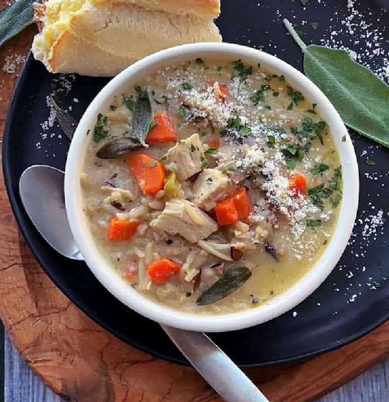 white bowl with leftover turkey wild rice soup garnished with parmesan cheese served with hunk of bread