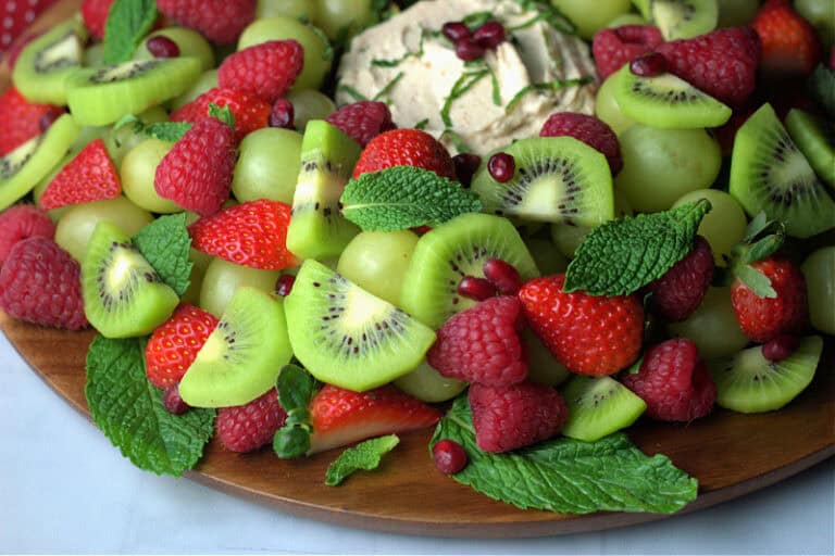 round wood cutting board with christmas fruit wreath (fruit shaped like a wreath garnished with mint leaves