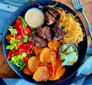 overhead view - black bowl with burger bowls with lettuce, tomato, shredded cheese, sweet potato fries and burger sauce.