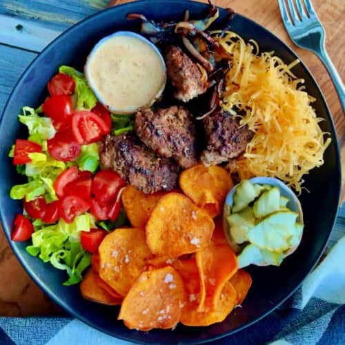 overhead view - black bowl with burger bowls with lettuce, tomato, shredded cheese, sweet potato fries and burger sauce.
