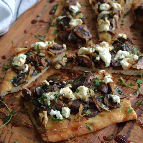 wooden board with mushroom goat cheese flatbread cut in squares, drizzled with balsamic vinegar