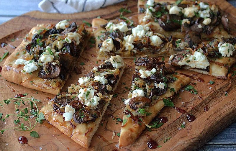 wooden board with mushroom goat cheese flatbread drizzled with balsamic glaze