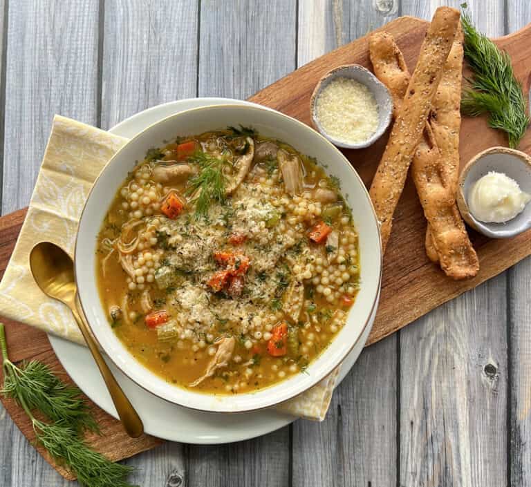 overhead view - bowl of chicken pastina soup with breadsticks and butter