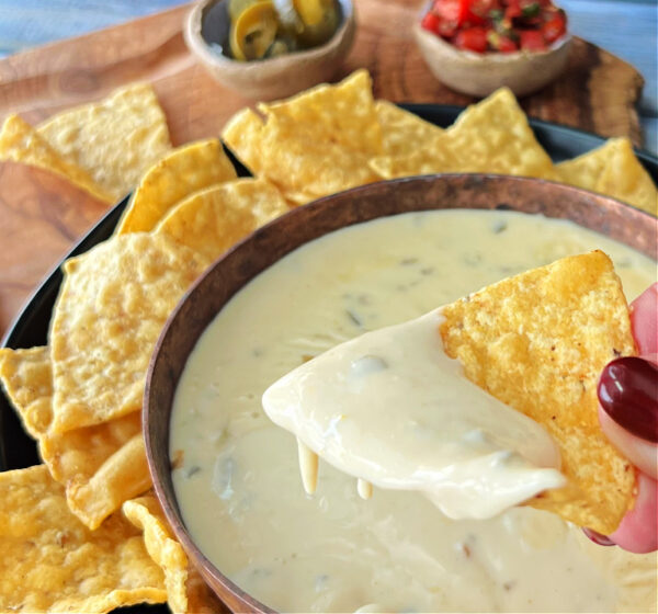 closeup of tortilla chip scooping slow cooker nacho cheese sauce from bowl.