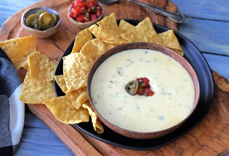 brown bowl filled with slow cooker nachocheese sauce surrounded by tortilla chips