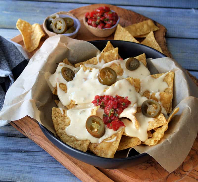 black bowl with tortilla chips and slow cooker nacho cheese sauce over the top, garnished with pico de gallo
