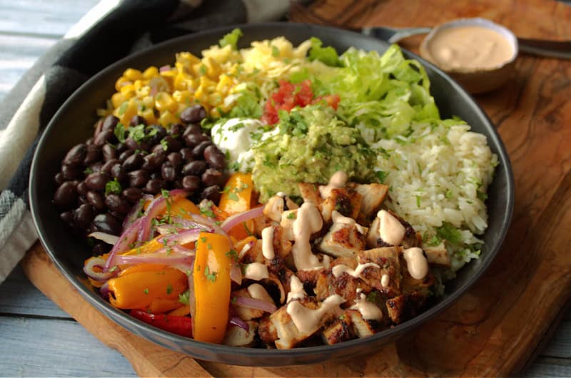 chicken burrito bowl in a black bowl with small container of sauce