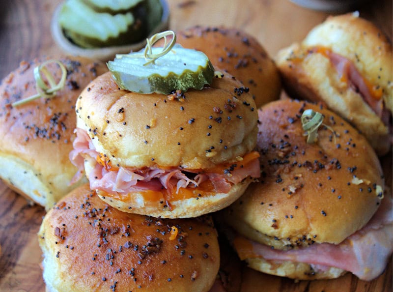 baked ham and cheese sliders stacked on wood cutting board
