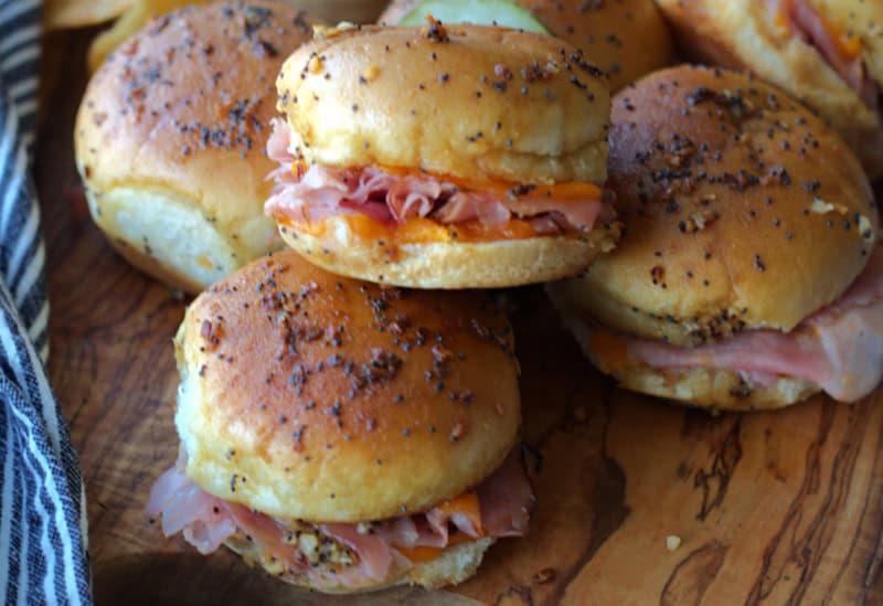 ham and cheese sliders stacked on wood cutting board with pickles