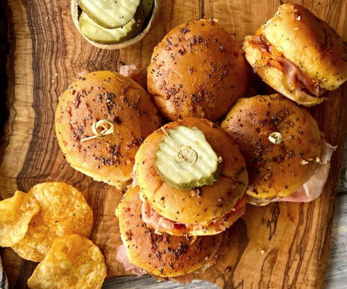 overhead view of baked ham and cheese sliders topped with pickle chips on a cutting board