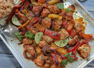 closeup of sheet pan chicken fajitas with chicken, bright bell peppers, onions and slices of lime for garnish