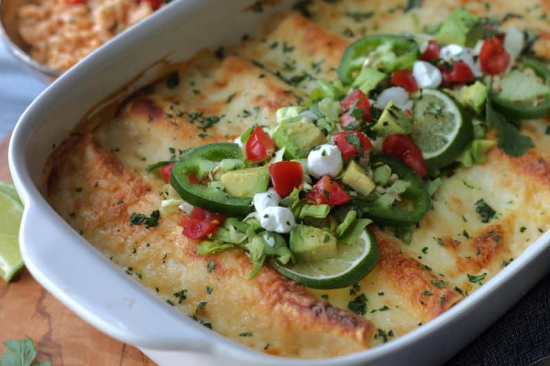 closeup - white casserole dish with white chicken enchiladas garnished with tomatoes and diced avocado