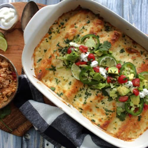 white casserole dish with white chicken enchiladas garnished with diced tomatoes, avocado and cilantro