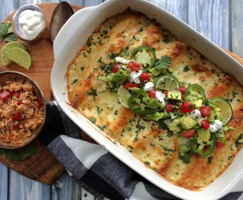 white casserole dish with white chicken enchiladas garnished with diced tomatoes, avocado and cilantro