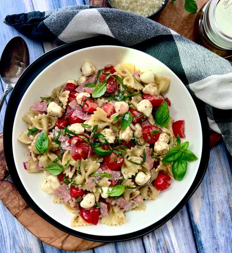 overhead view white bowl with caprese pesto pasta salad garnished with fresh basil leaves