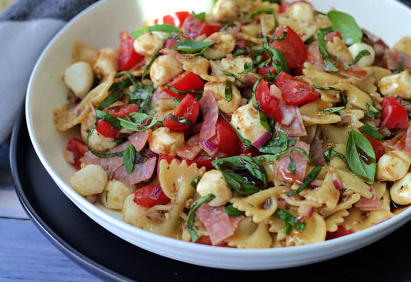 white bowl with caprese pesto pasta salad garnished with fresh basil leaves