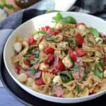 white bowl with caprese pesto pasta salad garnished with fresh basil leaves