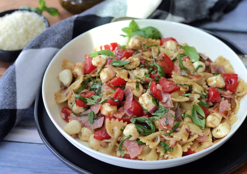 white bowl with caprese pesto pasta salad garnished with fresh basil leaves