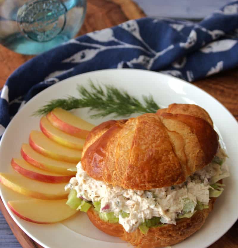 white plate with classic chicken salad on a croissant served with sliced apples