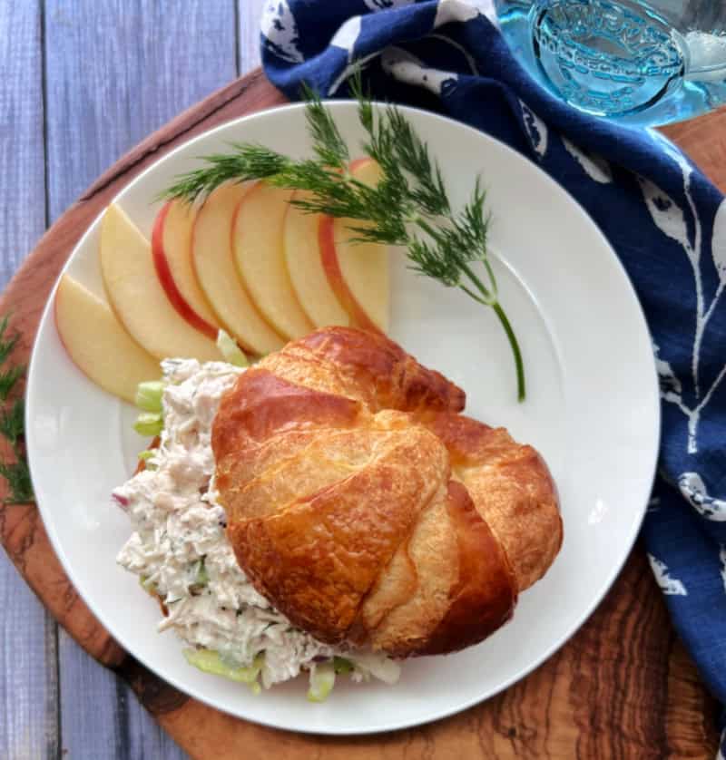 overhead view white plate with classic chicken salad on croissant and sliced apples on the side