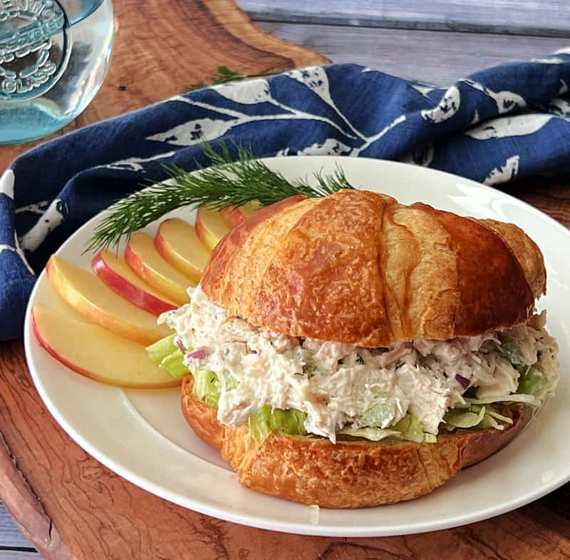 white plate with classic chicken salad on croissant with sliced apples on the side