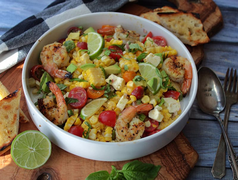 overhead view white bowl with corn salad garnished with lime slices and fresh basil