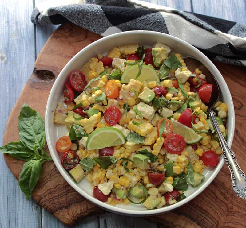overhead view - white bowl with corn salad garnished with lime sliced and fresh basil