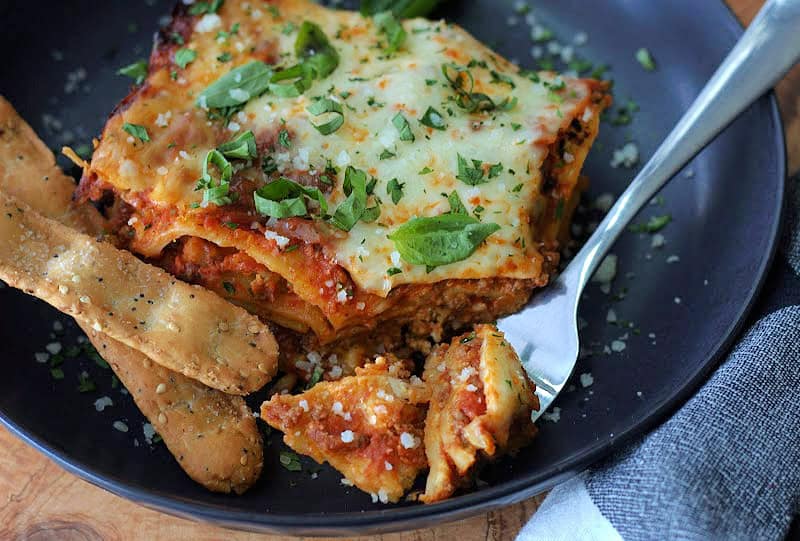 black plate with slow cooker lasagna and forkful of it.
