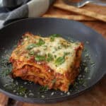 black plate with slice of slow cooker lasagna garnished with sliced basil