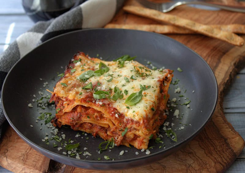 black plate with slice of slow cooker lasagna garnished with sliced basil