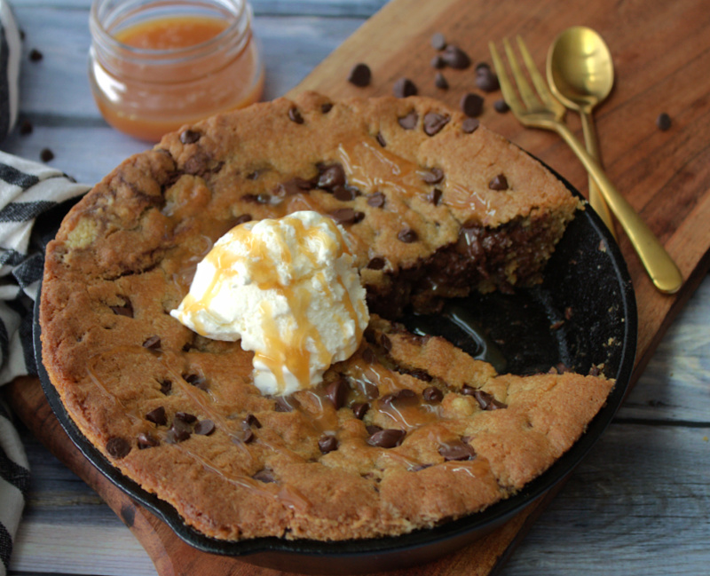 skillet chocolate chip cookie in cast iron skillet with wedge sliced out and topped with scoop of vanilla ice cream