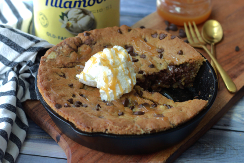 skillet chocolate chip cookie in black cast iron skillet with wedge removed and topped with scoop of vanilla ice cream.