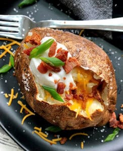 overhead view air fryer baked potatoes topped with sour cream, cheese and bacon bits