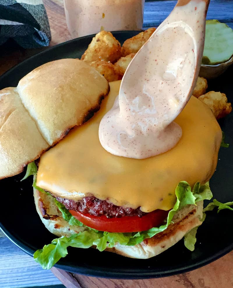 cheeseburger with a spoon dripping burger sauce onto it