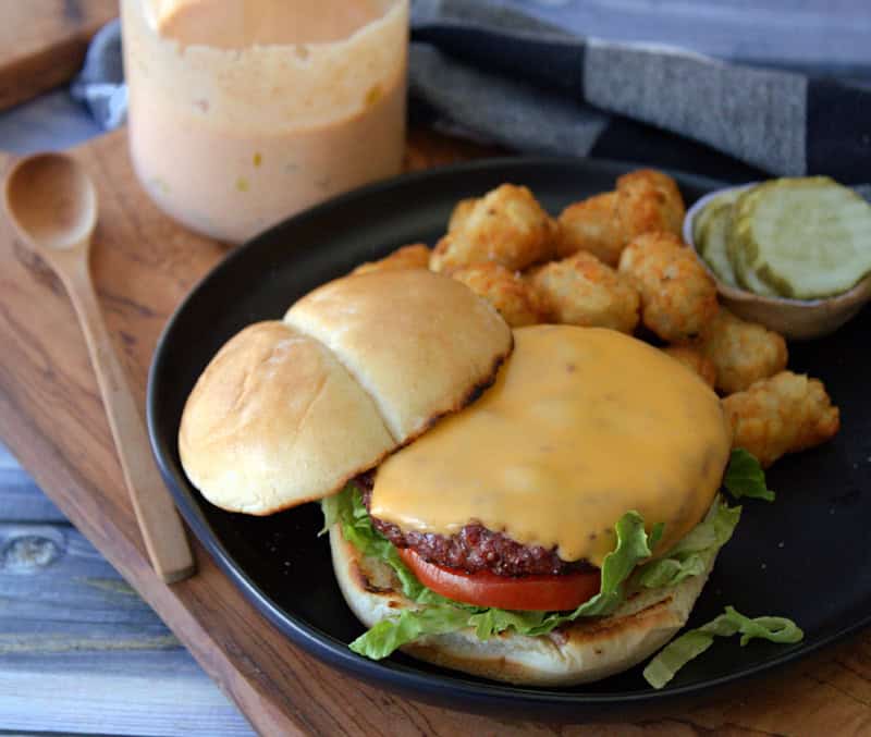 cheeseburger on a plate with tater tots and jar of burger sauce on the side