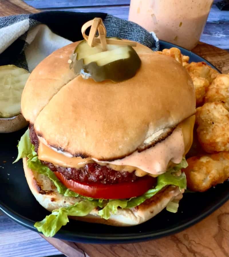 cheeseburger with burger sauce running down the side of it and tater tots on the side.