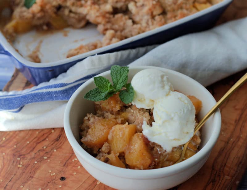 bowl with peach cobbler topped with scoops of vanilla ice cream and fresh mint leaves