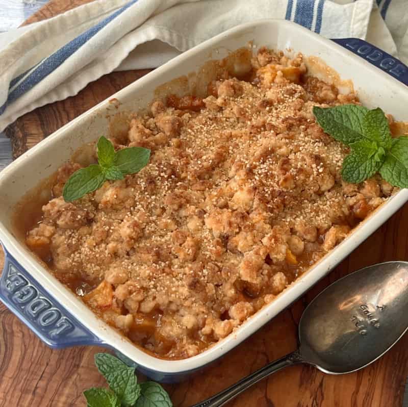 baking dish with peach cobbler garnished with a few fresh mint leaves