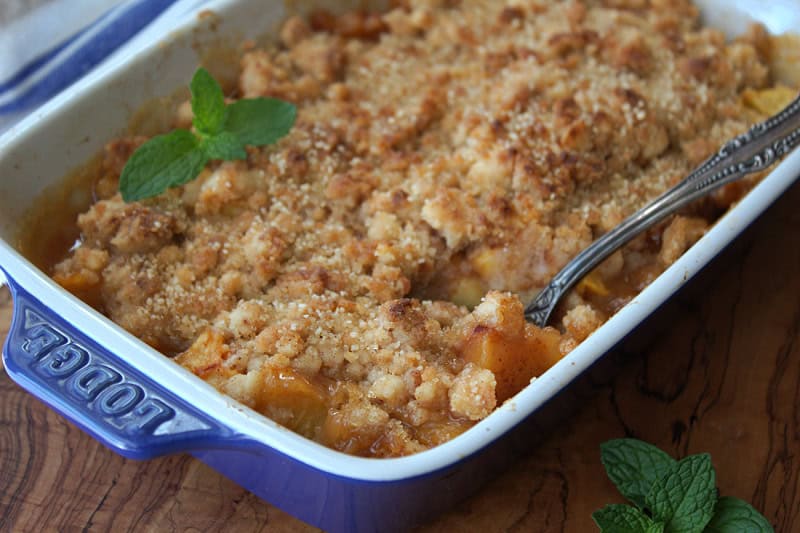 blue baking dish with peach cobbler garnished with a few fresh mint leaves