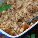 baking dish with peach cobbler garnished with a fresh mint leaf