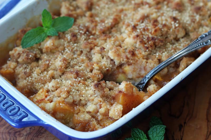 baking dish with peach cobbler garnished with a fresh mint leaf
