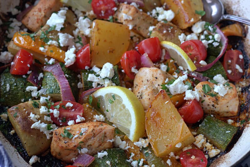 closeup of greek sheet pan chicken with crumbled feta and tomatoes