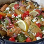 overhead view - greek sheet pan chicken in dutch oven garnished with lemon slices and crumbled feta cheese