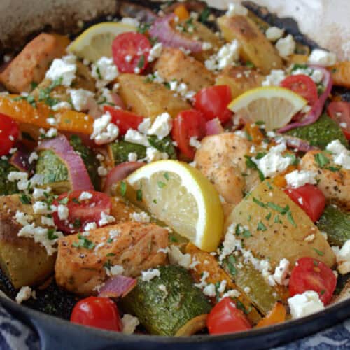 overhead view - greek sheet pan chicken in dutch oven garnished with lemon slices and crumbled feta cheese