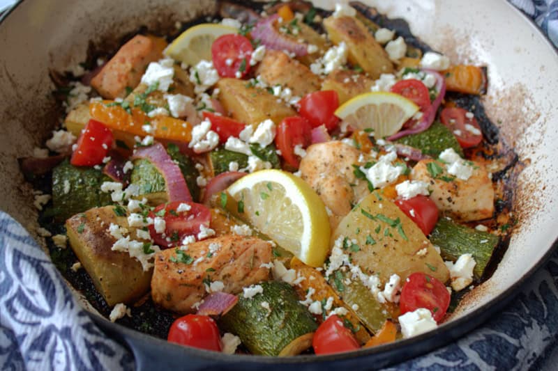 overhead view - greek sheet pan chicken in dutch oven garnished with lemon slices and crumbled feta cheese