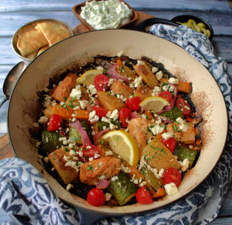 Greek Sheet Pan Chicken in a dutch oven with a bowl of tzatzi next to it.