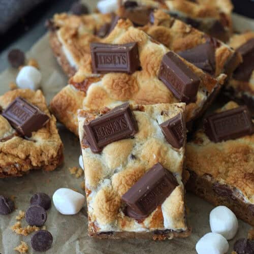 smores cookies bars squares on parchment paper with a few mini marshallows around them.
