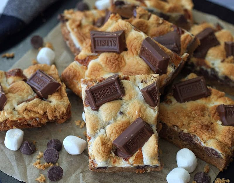smores cookies bars squares on parchment paper with a few mini marshallows around them.