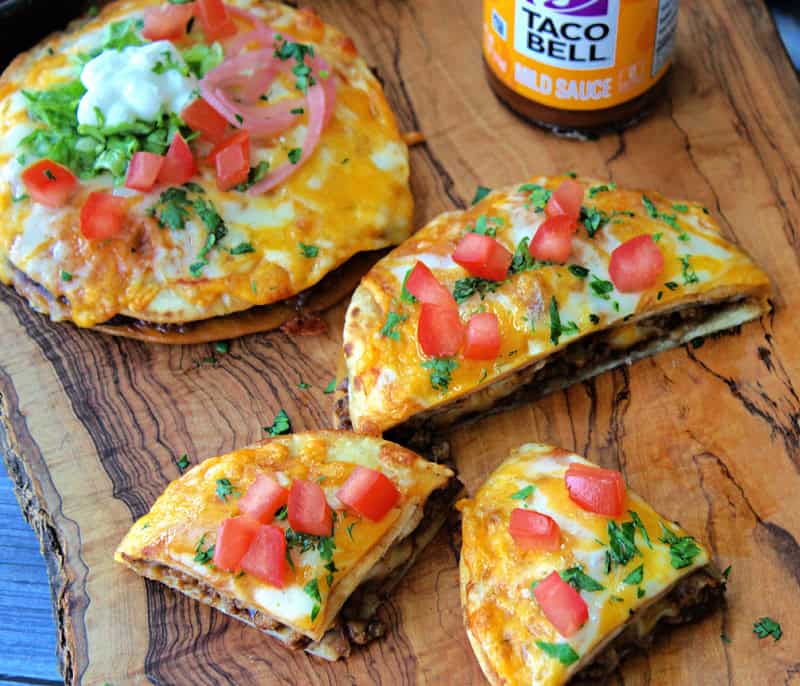 wood board with mexican pizzas - one whole and one cut in wedges.