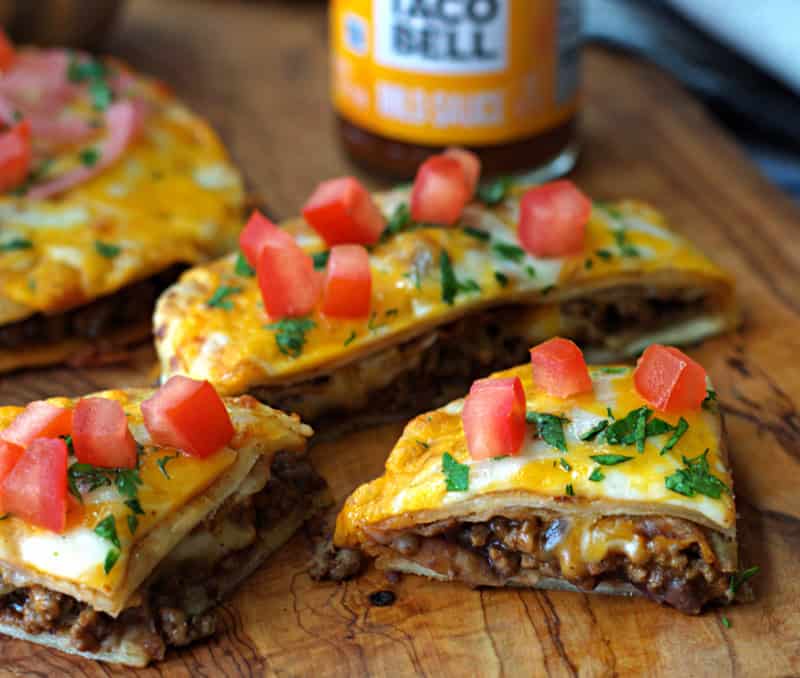 wood board with mexican pizza cut in wedges and taco bell taco sauce in background